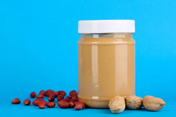 Köstliche Erdnussbutter im Glas Erdnuss in der Nähe auf blauem Hintergrund — Stockfoto