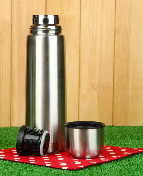 Metal thermos on grass on wooden background — Stock Photo, Image