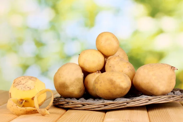 Ripe potatoes on wicker cradle on wooden table on natural background — Stock Photo, Image