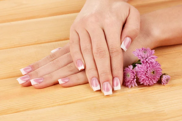 Frau Hände mit französischer Maniküre und Blumen auf hölzernem Hintergrund — Stockfoto