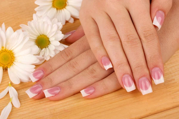 Mãos de mulher com manicure francês e flores em fundo de madeira — Fotografia de Stock