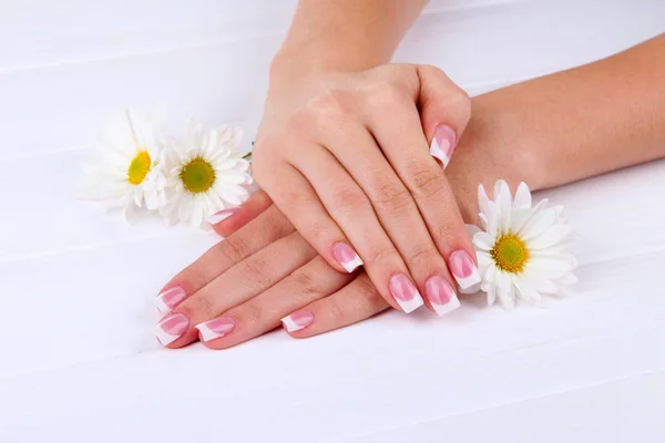 Manos de mujer con manicura francesa y flores sobre fondo de madera blanca —  Fotos de Stock