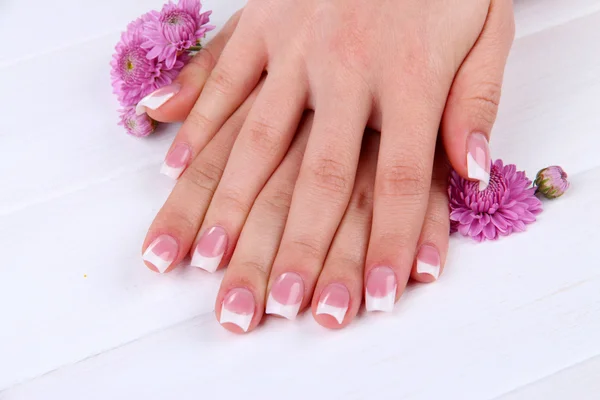 Manos de mujer con manicura francesa y flores sobre fondo de madera blanca —  Fotos de Stock