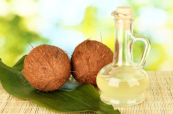 Графин с кокосовым маслом и кокосами на зеленом фоне — стоковое фото
