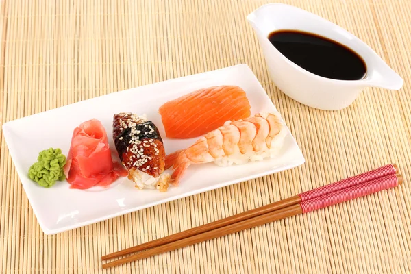 Delicious sushi served on plate on bamboo mat — Stock Photo, Image