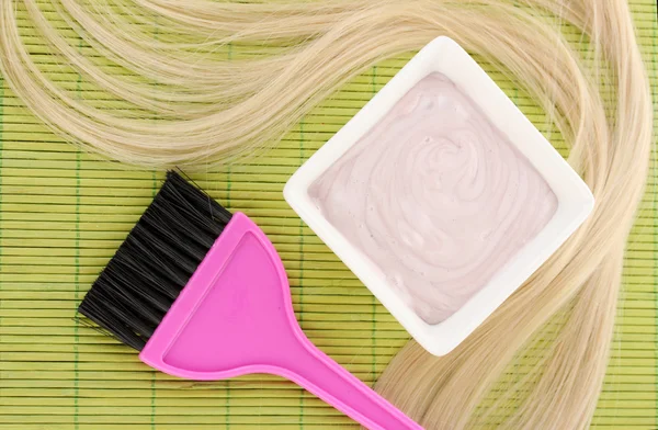 Tinte para el cabello en un tazón y cepillo para la coloración del cabello en una esterilla de bambú verde, primer plano — Foto de Stock