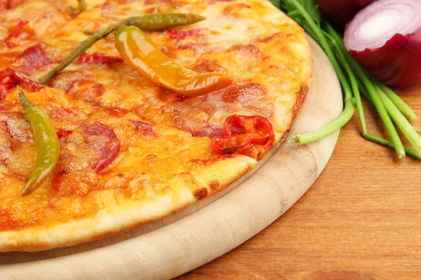 Tasty pepperoni pizza with vegetables on wooden board on wooden background — Stock Photo, Image