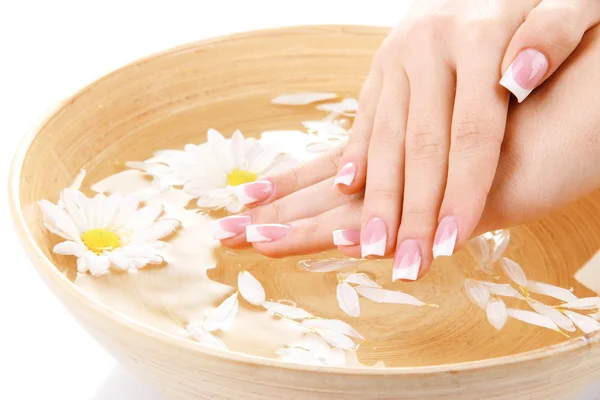 Mãos de mulher com manicure francês e flores em tigela de bambu com água — Fotografia de Stock