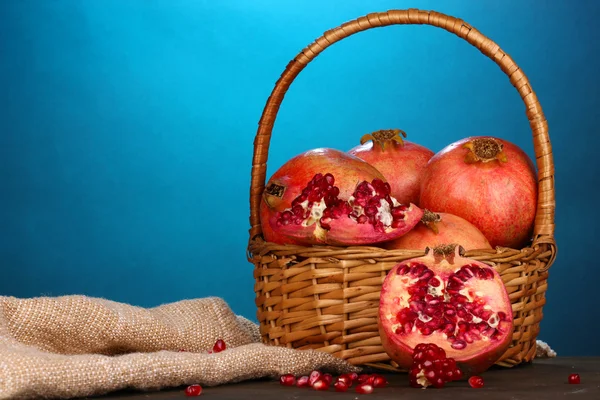 Ripe pomegranates on basket on wooden table on blue background — Stock Photo, Image