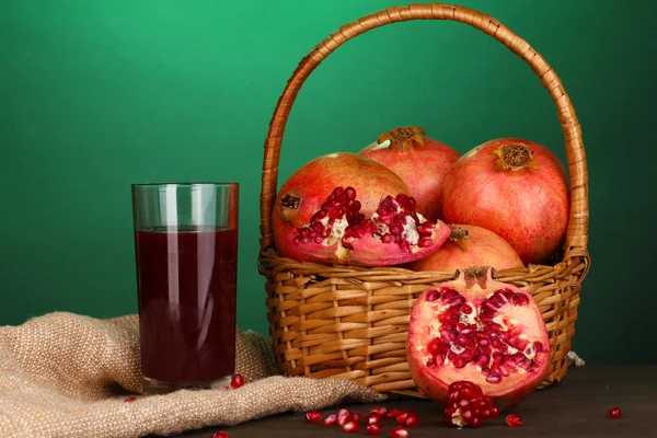 Reife Granatäpfel auf Korb mit Glas Granatapfelsaft auf Holztisch — Stockfoto