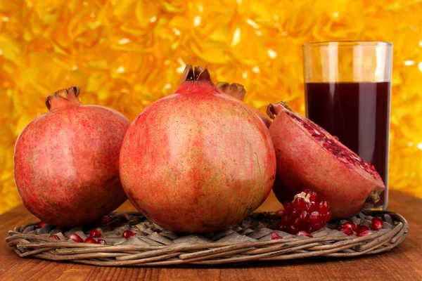 Ripe pomegranates on wicker cradle with glass of pomegranate juice on woode — Stock Photo, Image