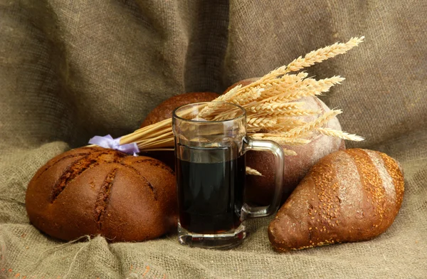 Tankard of kvass and rye breads with ears, on burlap background — Stock Photo, Image