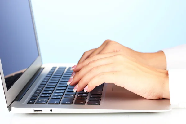 Hands typing on laptop keyboard close up on blue background Stock Image