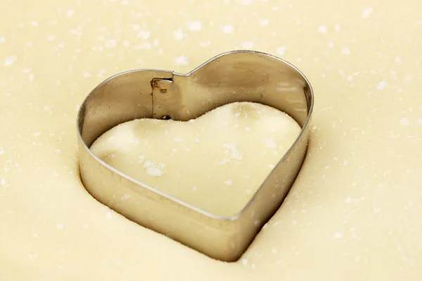 Cutter in the shape of a heart on the rolled out dough close-up — Stock Photo, Image