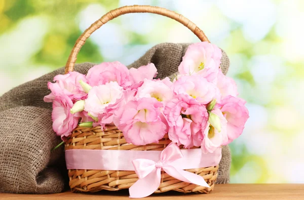 Bouquet of eustoma flowers in basket, on wooden table, on green background — Stock Photo, Image