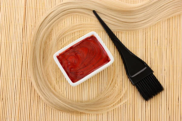 Hair dye in bowl and brush for hair coloring on beige bamboo mat, close-up — Stock Photo, Image