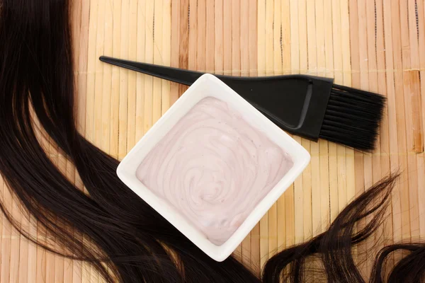 Tintura per capelli in ciotola e pennello per la colorazione dei capelli su tappetino di bambù beige, primo piano — Foto Stock