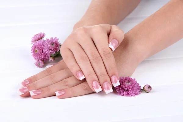 Mãos de mulher com manicure francês e flores em fundo de madeira branca — Fotografia de Stock