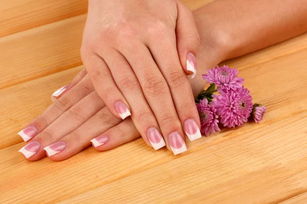 Mãos de mulher com manicure francês e flores em fundo de madeira — Fotografia de Stock