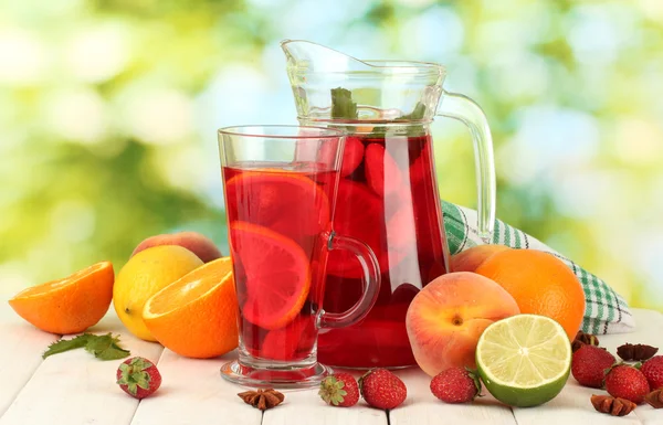 Sangria in jar and glass with fruits, on wooden table, on green background — Stock Photo, Image