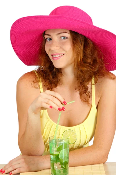 Sonriente hermosa chica sentada en la mesa con sombrero de playa y cóctel iso —  Fotos de Stock