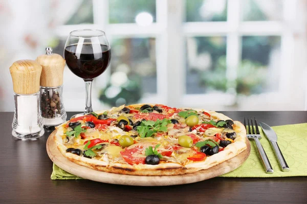 Delicious pizza with glass of red wine and spices on wooden table on window — Stock Photo, Image