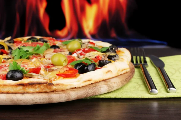 Delicious pizza close-up on wooden table on fire background — Stock Photo, Image