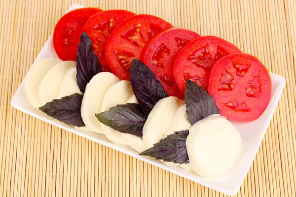 Mozzarella saporita con pomodori su piatto su tappetino — Foto Stock