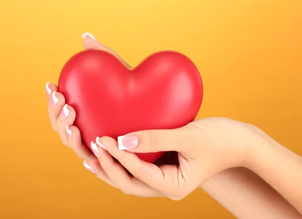 Coração vermelho nas mãos da mulher, no fundo laranja close-up — Fotografia de Stock
