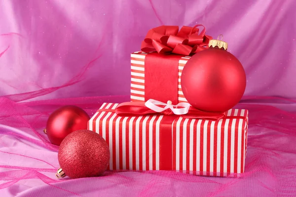 Coloridos regalos rojos con lazo y bolas de Navidad sobre fondo rosa — Foto de Stock