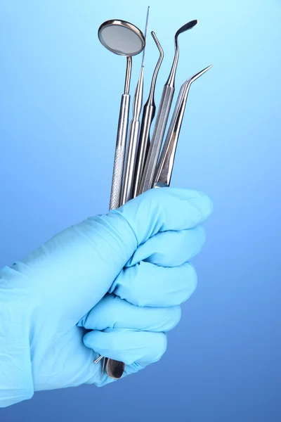 Hand in blauem Handschuh mit Zahnwerkzeugen auf blauem Hintergrund — Stockfoto