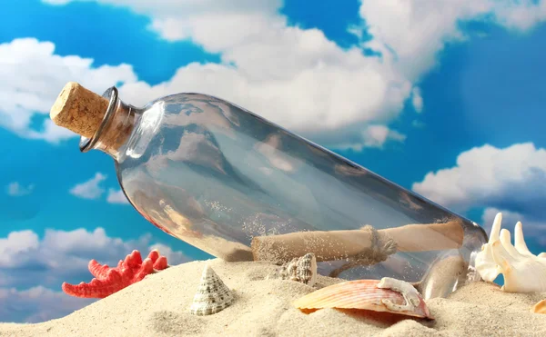 Glass bottle with note inside on sand, on blue sky background — Stock Photo, Image