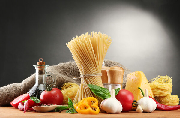 Pasta spaghetti, vegetables and spices, on wooden table, on grey background