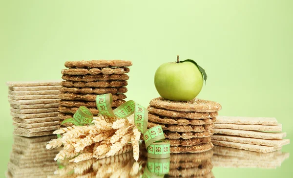 Tasty crispbread, apple, measuring tape and ears, on green background — Stock Photo, Image