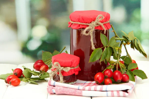 Jarros com geléia de rosas quadril e bagas maduras, na mesa de madeira — Fotografia de Stock