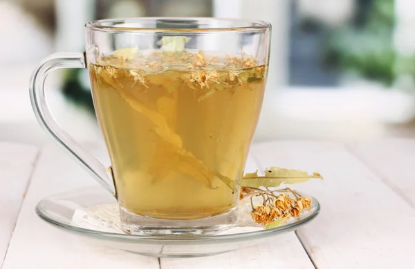 Glass cup of tea with linden on wooden table on window background — Stock Photo, Image