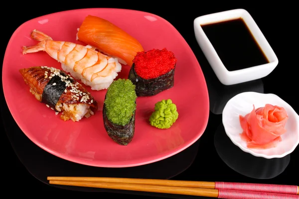 Heerlijke sushi geserveerd op rode plaat geïsoleerd op zwart — Stockfoto