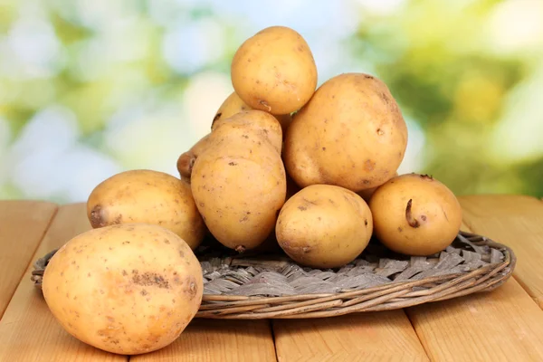 Batatas maduras no berço de vime na mesa de madeira no fundo natural — Fotografia de Stock