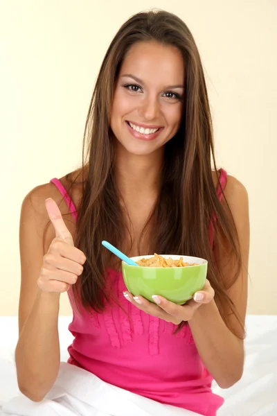 Jonge mooie vrouw met kom cornflakes in bed — Stockfoto