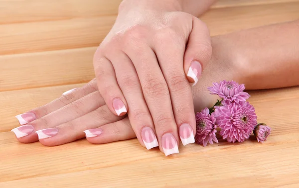 Mãos de mulher com manicure francês e flores em fundo de madeira — Fotografia de Stock