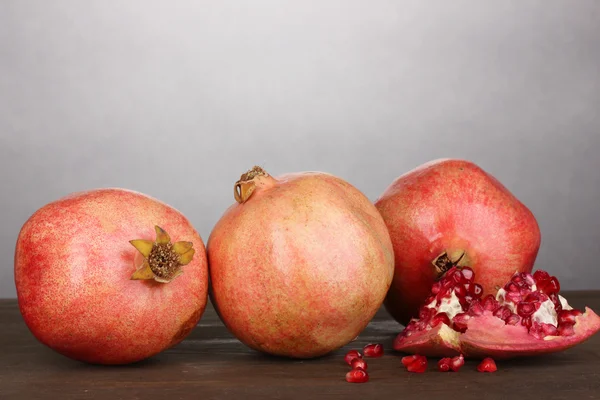 Ripe pomegranates on wooden table on grey background — Stock Photo, Image