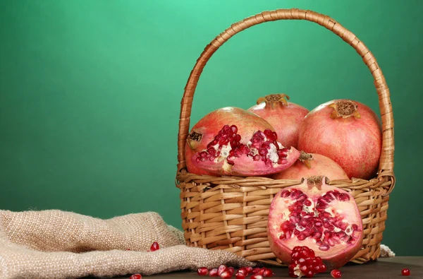 Ripe pomegranates on basket on wooden table on green background — Stock Photo, Image