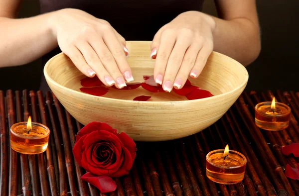 Manos de mujer con cuenco de madera de agua con pétalos — Foto de Stock