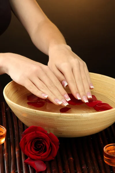 Manos de mujer con cuenco de madera de agua con pétalos, sobre fondo marrón —  Fotos de Stock