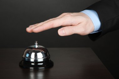 Hand ringing in service bell on wooden table on black background clipart