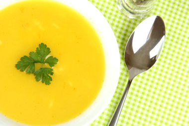 Yeşil masa örtüsü üzerinde beyaz tabak içinde kokulu çorba