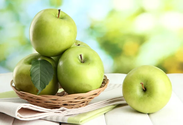 Ripe green apples with leaves in basket, on wooden table