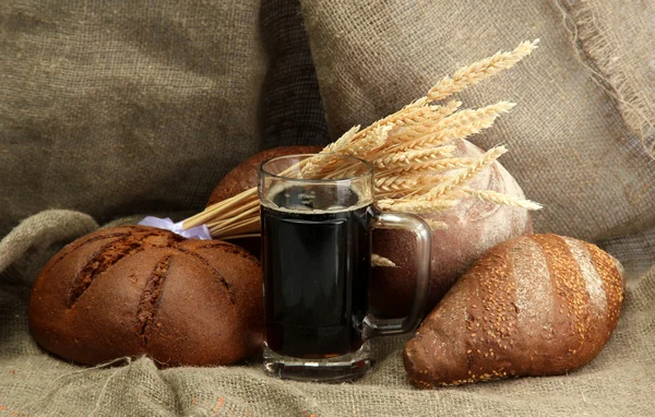 Tankard of kvass and rye breads with ears, on burlap background — Stock Photo, Image