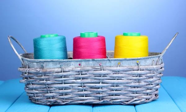 Bright threads in basket on wooden table on blue background — Stock Photo, Image