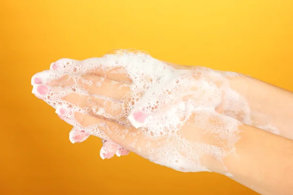 Tangan wanita di soapsuds, di latar belakang oranye close-up — Stok Foto